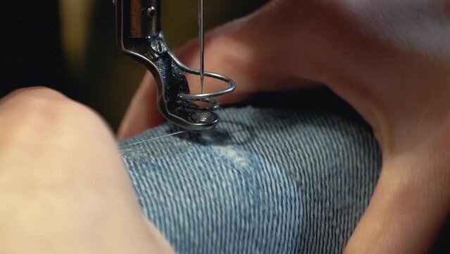 A female tailor seamstress repair old jeans with vintage darning machine in a workshop repairing denim clothes. Small family business, tailoring and repair of clothes, handmade, startup. Close-up
