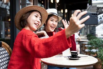 Happy smiling Asian woman selfie on her smartphone, sitting at older cafe with beverage. Winter...