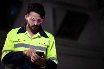 Handsome engineer using smartphone for control fluorescent smart digital glasses with futuristic holographic interface to display data and repair defects of equipment in the factory.