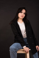 Portrait of an Armenian brunette girl in a black jacket on a black background.