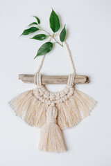 Beautiful macrame on stick hanging on a white wall, decorated with leaves.