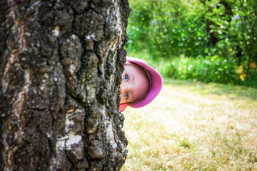Timid little blue-eyed girl looking out from behind a tree.