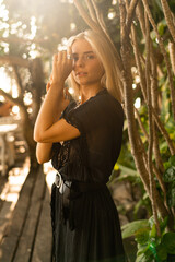 Fototapeta premium Close up portrait of pretty blond woman in boho stylish outfit posing outdoor in tropical garden. Stylish bohemian accessories.