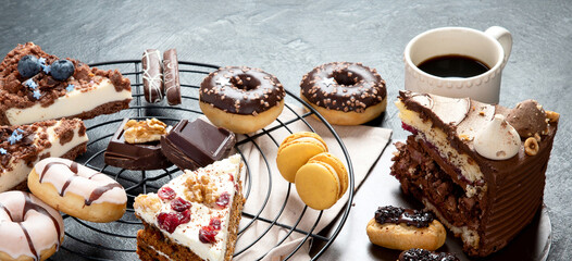 Table with various cookies, donuts, cakes, cheesecakes on dark background.