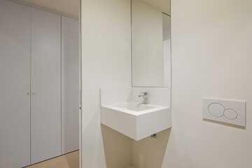 Modern simple bathroom with small sink, mirror and wardrobe in the background