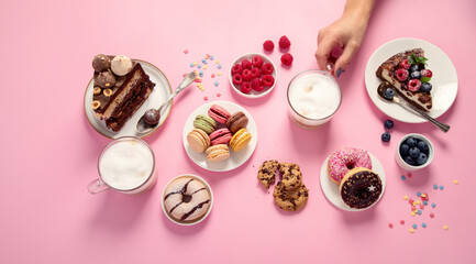 Obraz na płótnie Canvas Table with various cookies, donuts, cakes, coffee cups on pink background.