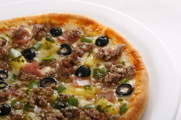 Closeup of single serve pizza with ground beef, olives, pineapple, cheese, ham, bell peppers