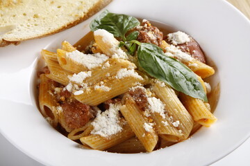 Closeup of penne pasta dish with grated parmesan, basil leaves and toast