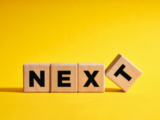 The word Next on wooden cubes with yellow background. Next level or step in business or education...