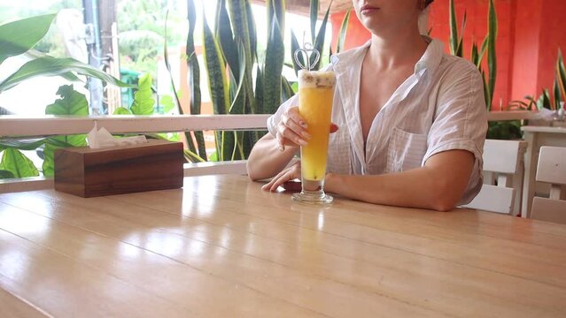 A girl drinks a cocktail of fruits in a cafe, a shake of passion fruit
