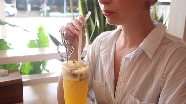 A girl drinks a cocktail of fruits in a cafe, a shake of passion fruit