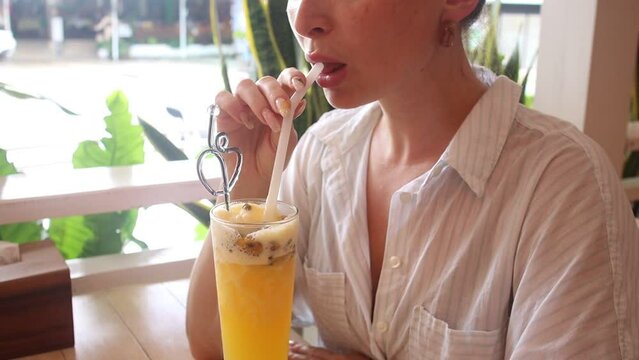 A girl drinks a cocktail of fruits in a cafe, a shake of passion fruit