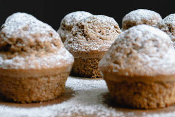Close-up of a baked chocolate cupcake on a wooden board and sprinkled with white powdered sugar surrounded by other cupcakes