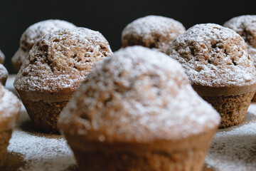 Close-up of a baked chocolate cupcake on a wooden board and sprinkled with white powdered sugar surrounded by other cupcakes