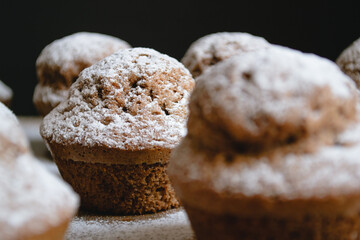 Close-up of a baked chocolate cupcake on a wooden board and sprinkled with white powdered sugar surrounded by other cupcakes