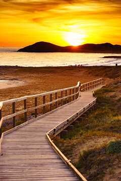 Sunset over beach with wooden path to sea water.