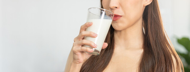 Happy, asian young woman, girl drinking a glass of white fresh, warm or hot dairy milk for calcium, vitamin wholesome good nutrition in morning at kitchen home. lifestyle, product healthy people.