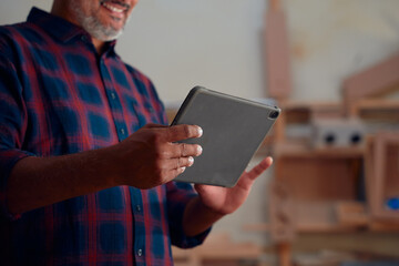 Close-up of mid adult man in checked shirt smiling while using digital tablet at woodworking factory