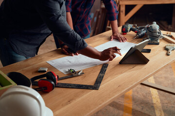 Close-up of men working over table with digital tablet and tools in woodworking factory