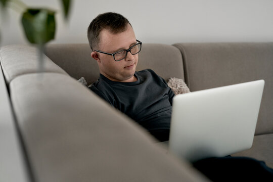 Man with down syndrome using laptop at home while sitting on sofa