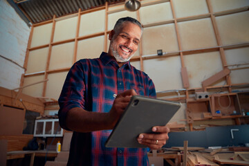 Mid adult man smiling while using digitized pen on digital tablet at woodworking factory