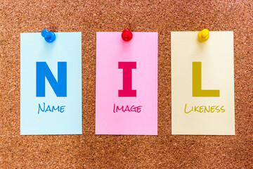 Conceptual 3 letters keyword NIL (Name, Image and Likeness) on multicolored stickers attached to a cork board.