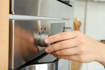 Young woman hand turn on oven, close up