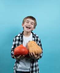 A laughing blond boy holds two pumpkins of different varieties in his hands. Portrait, copy of the space.