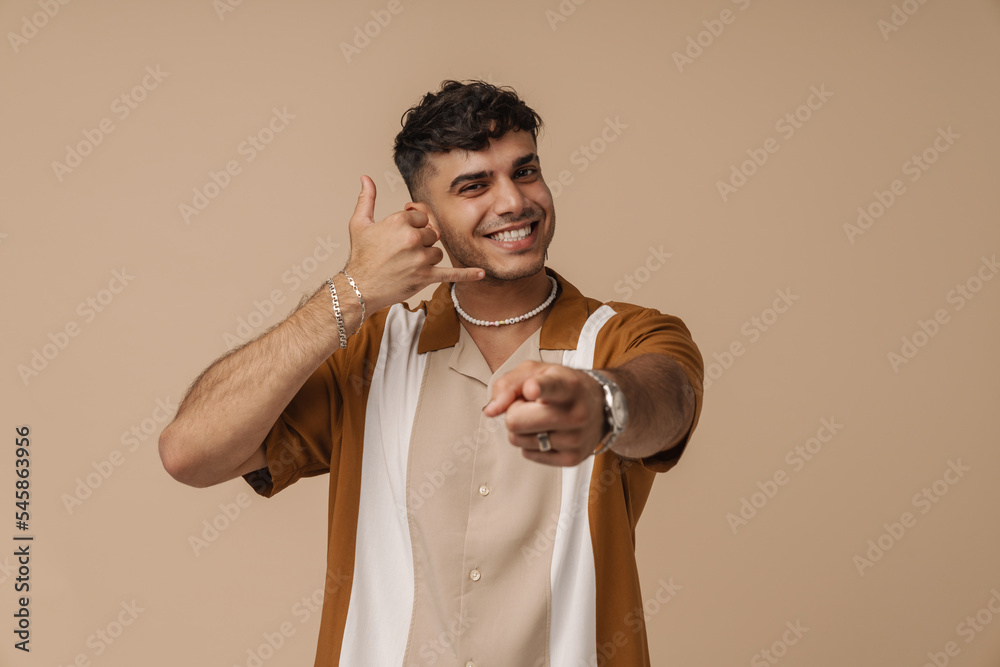 Wall mural Young handsome stylish smiling man doing phone gesture wit hand