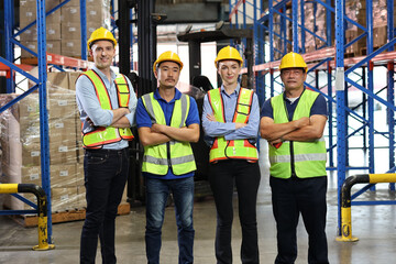 Group of warehouse workers with hardhats and reflective jackets standing and crossed arms with confident celebrate successful together or completed deal at retail warehouse logistics center