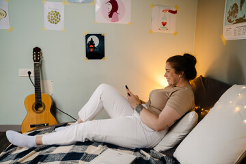 Young smiling girl in headphones with phone lying on bed