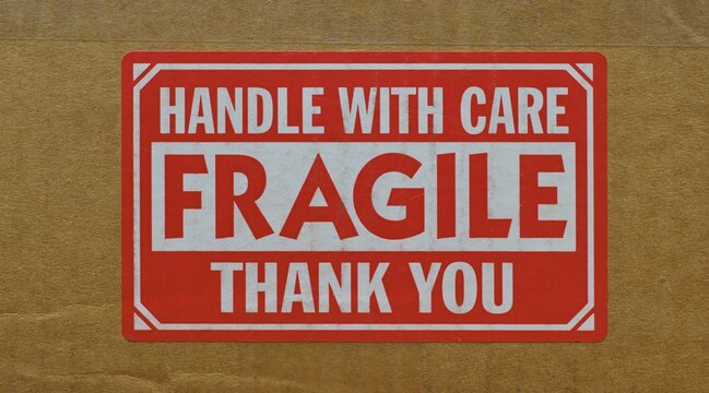Handle with care sticker attached to the side of a cardboard box. Closeup isolated front view and centered image.