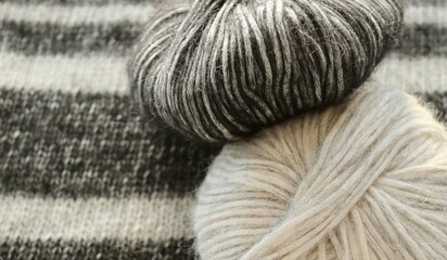Texture or background in the form of a knitted knitting cloth of contrasting stripes and two skeins of yarn on top of gray and black 