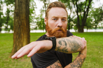 Adult handsome bearded tattooed redhead serious man stretching arm