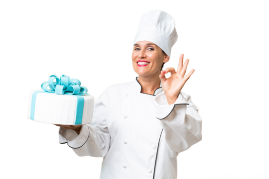 Middle-aged chef caucasian woman with a big cake over isolated background showing ok sign with fingers