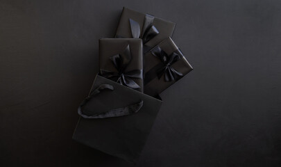 Gift box wrapped in black paper with a black bow in a package on a dark background. Holiday concept. Place for text or advertising. Christmas. Black Friday.