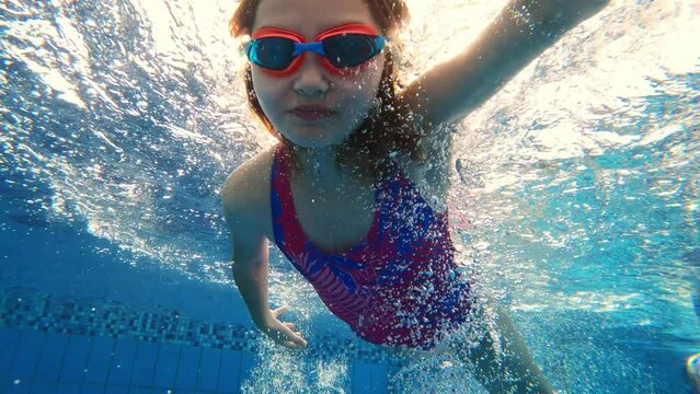 Cute little girl with goggles diving and swimming underwater in a pool