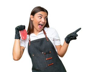 Butcher woman wearing an apron and serving fresh cut meat isolated on green chroma background pointing finger to the side and presenting a product