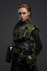 Shot of military woman with brown hairs and gas mask dressed in camouflage costume.