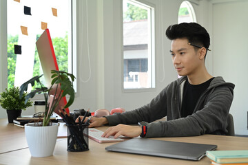 Focused young asian man working on design project with personal computer at graphic studio