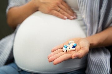 Portrait of pregnant woman holding pill. Woman taking vitamin.