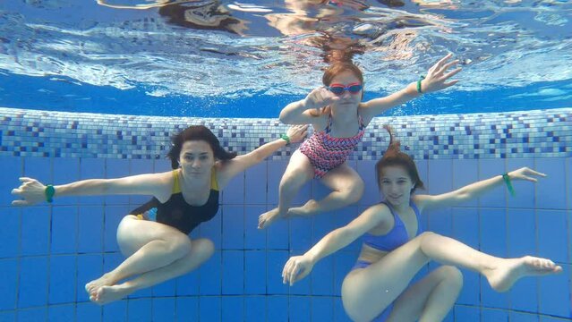 Mother and her dauthters swimming underwater in a swimming pool. Girls have a fun in a water.