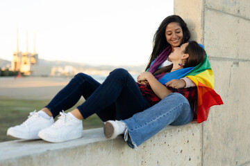 Happy lesbian young couple embraces and holds a rainbow flag. LGBT community.