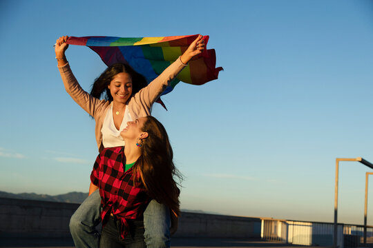 Happy lesbian young couple embraces and holds a rainbow flag. LGBT community. - Powered by Adobe