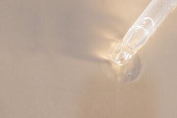 Shining pipette dropper  with transparent liquid drops on beige  background with sun reflection.  Concept for  Health and beauty