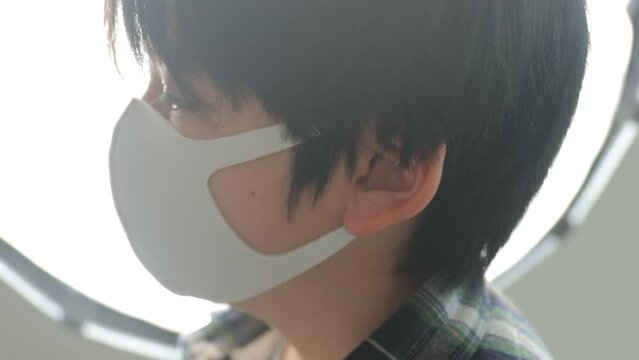 Profile shot of young asian boy wearing a mask in front of light.