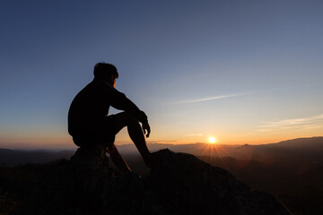 silhouette of Sad man sitting alone on top of a mountain at sunset, Depression and loneliness.  The...