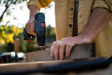 Close-up of handyman carpenter working in carpentry diy workshop outdoors with drill.