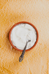 Turkish yogurt in a clay bowl with a spoon in it, top view flat lay yogurt photo on yellow background