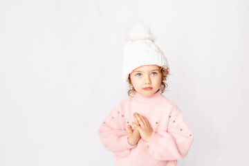 beautiful child girl on a white isolated background in a pink sweater folded cute pens as if praying, space for text